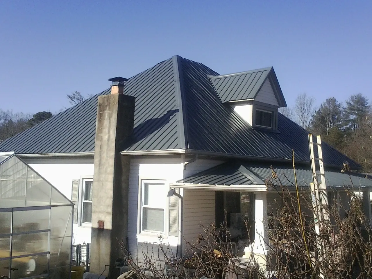 Dark blue standing seam metal roof on a white farmhouse with dormer — Slate & Tile Roof Repair by Roofing Brothers in Barnstead