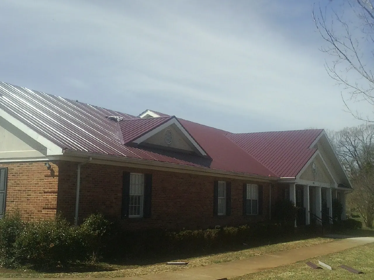Red metal roof with gabled entries on a long brick building, from a Hail Damage Roof Repair job in Barnstead