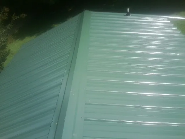 New green metal panels meeting at the ridge of a roof — Flat Roof Repair work by our crew in Barnstead