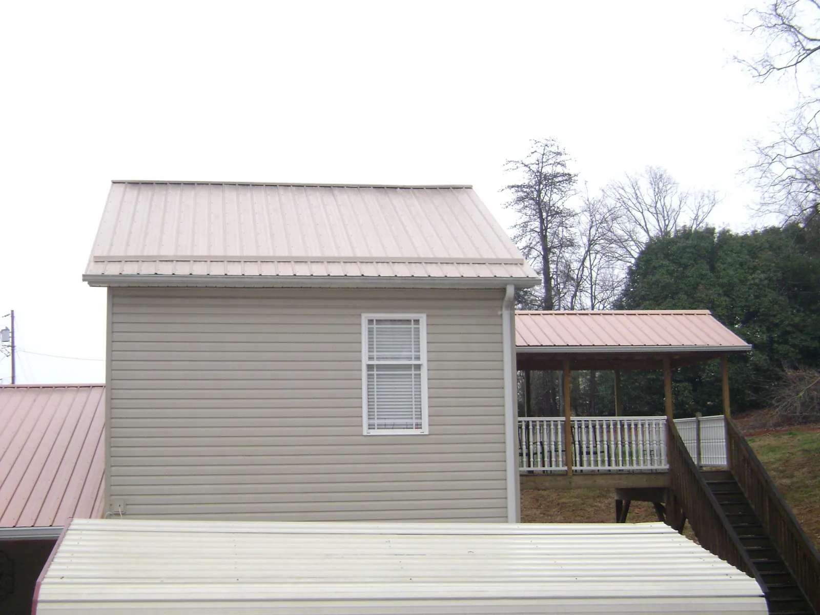 Tan metal roofs on a two story addition and attached porch, from a Roof Replacement job in Barnstead